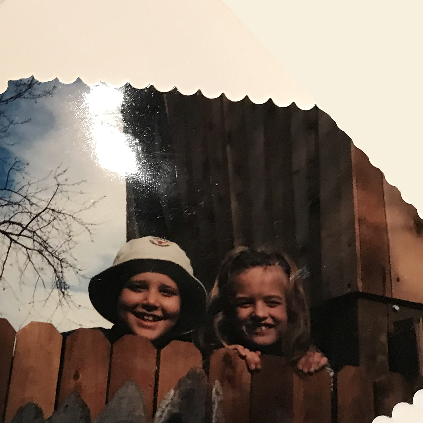Wesley Beckner and Camille Ritchie as children, peeking over a wooden fence